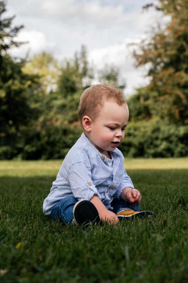 Kleines Kind sitzt auf einer grünen Wiese und spielt – authentisches Kinderportrait im Freien.