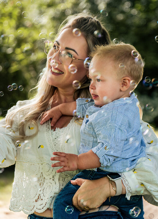Mutter hält ihr Kind im Arm, beide lächeln umgeben von Seifenblasen – liebevolles Familienshooting
