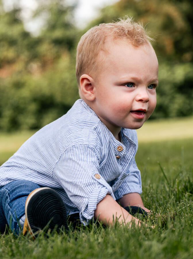 Kleines Kind sitzt auf einer grünen Wiese und spielt – authentisches Kinderportrait im Freien.
