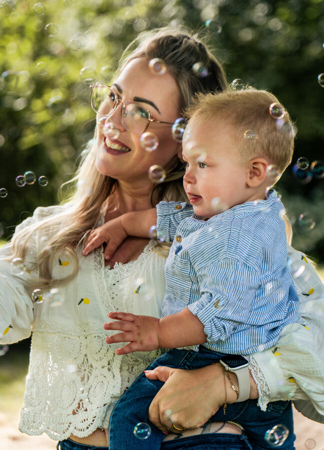 Mutter hält ihr Kind im Arm, beide lächeln umgeben von Seifenblasen – liebevolles Familienshooting