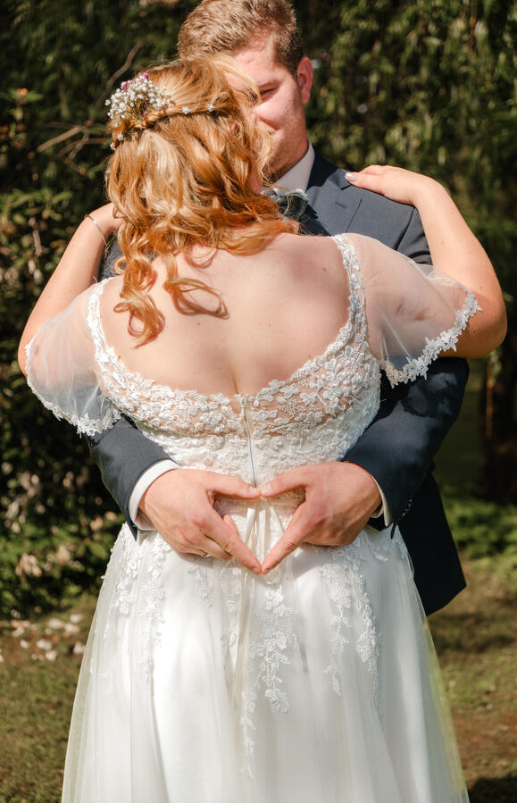 Hochzeitsdetails im Malepartus Bargteheide – Bräutigam formt ein Herz auf dem Rücken der Braut von MomentTraum Fotografie.