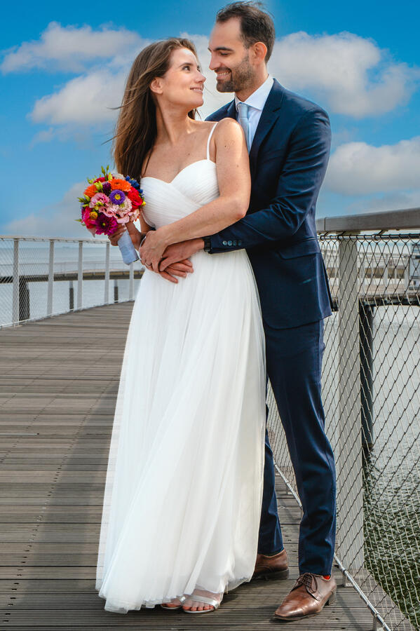 Brautpaar beim Hochzeitsshooting auf einer Brücke, Braut mit Strauß in inniger Umarmung