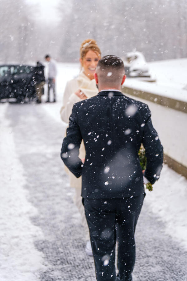 Bräutigam läuft im Schneefall auf seine lächelnde Braut zu, winterliche Hochzeitsaufnahme im Freien.