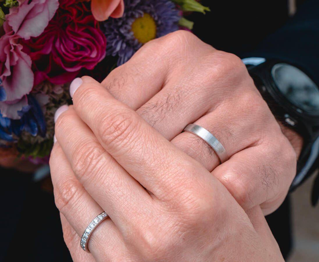 Nahaufnahme der Hände eines Brautpaars mit Ehering und Brautstrauß