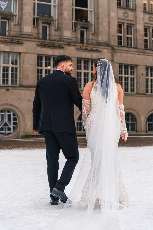Braut und Bräutigam gehen Hand in Hand im Schnee vor einem historischen Gebäude bei einer Hochzeit in Kiel