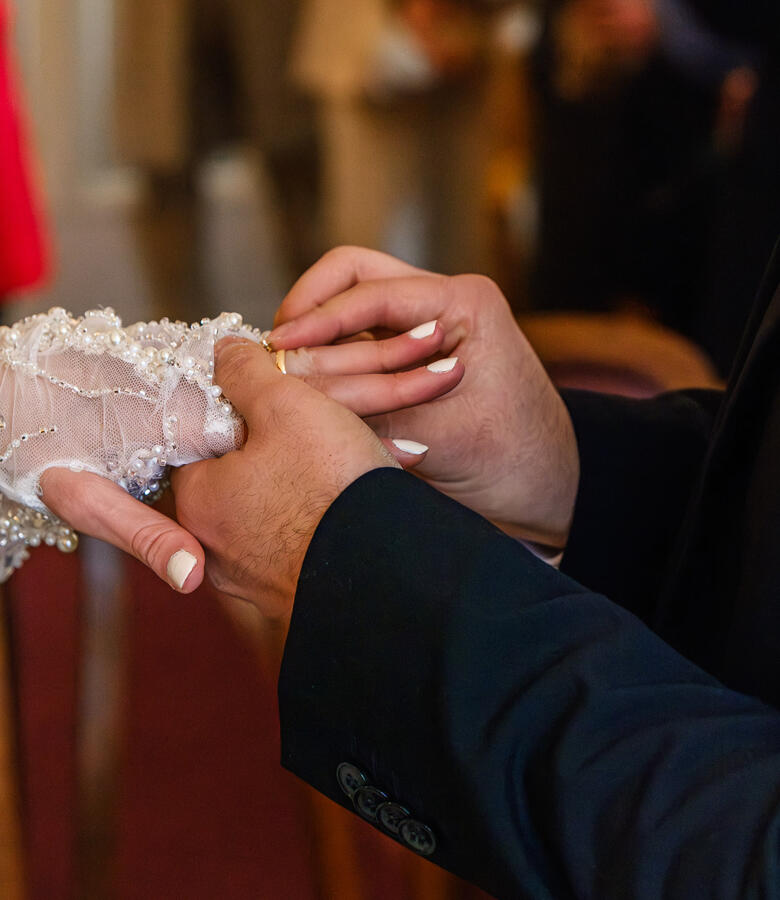 Braut und Bräutigam bei der Ringübergabe während einer Hochzeitszeremonie – Detailaufnahme der Hände mit Ehering