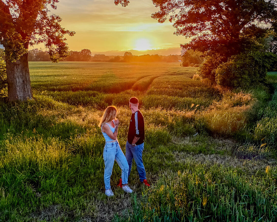 Luftaufnahme eines Pärchens bei Sonnenuntergang – romantisches Paarshooting mit Drohne zur goldenen Stunde auf einem Feld in Schleswig-Holstein