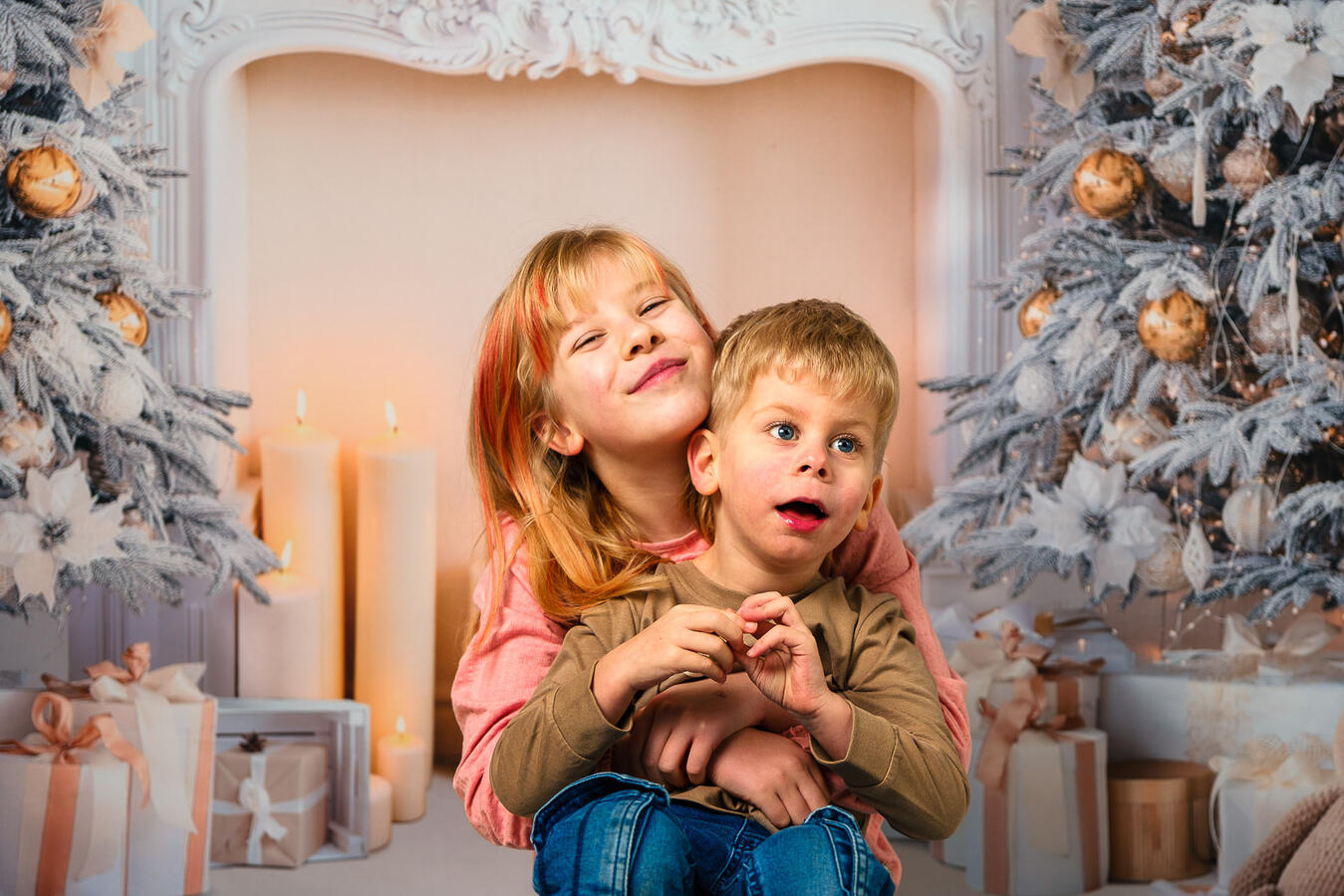 Zwei Kinder sitzen eng zusammen vor einer weihnachtlich dekorierten Hintergrundszene mit Kerzen und winterlicher Deko.
