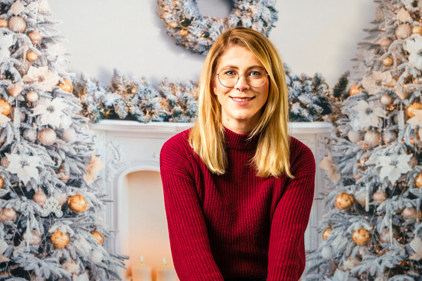 Person sitzt vor weihnachtlicher Dekoration mit Winterkränzen und hellem Hintergrund und lächelt ruhig in die Kamera.