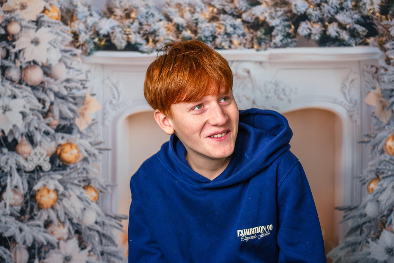 Portrait eines Jungen in blauem Pullover vor einer winterlichen Hintergrundkulisse. Ein natürlicher, ruhiger Moment aus einem Familienshooting, aufgenommen in weichem, stimmungsvollem Licht.