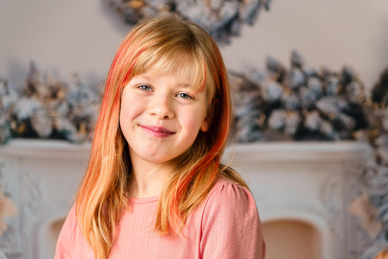 Porträt eines blondhaarigen Mädchens im rosa Pullover vor einer weichen, dekorativen Hintergrundszene.