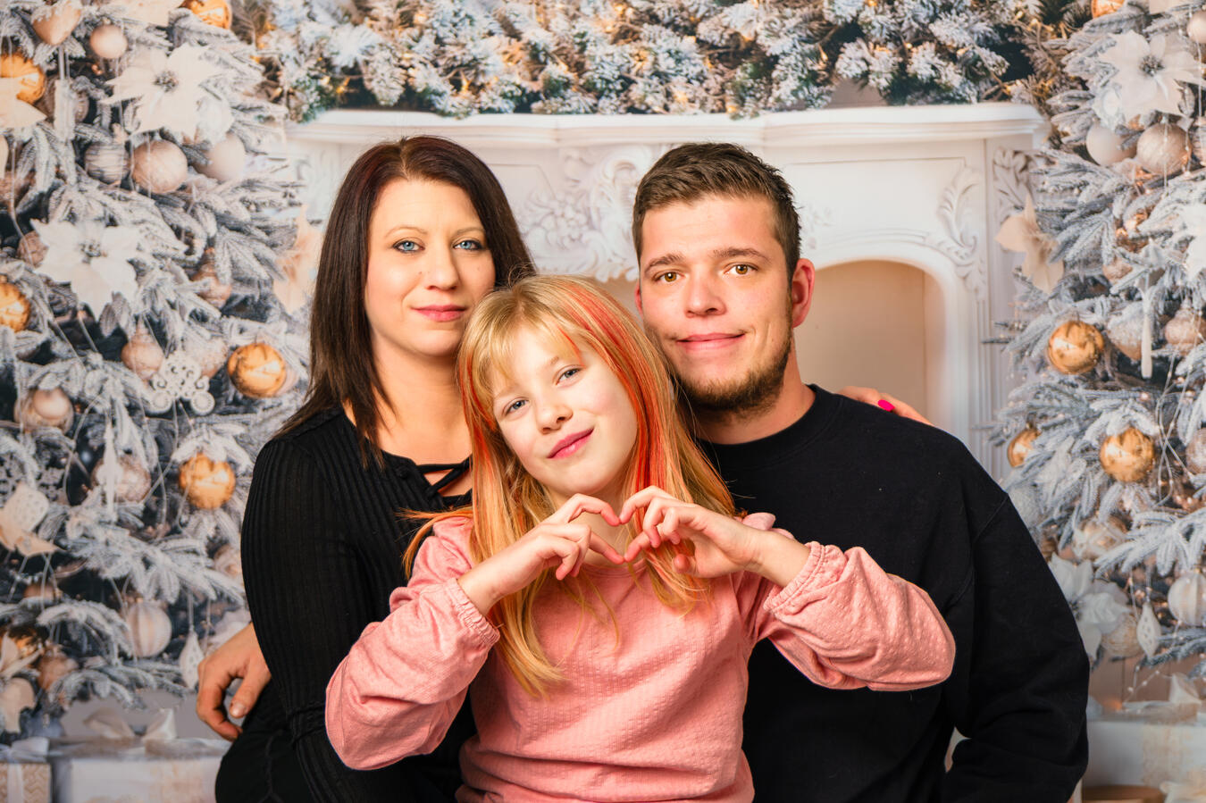 Familie sitzt gemeinsam vor einer weihnachtlich dekorierten Hintergrundszene mit Kerzen und winterlicher Deko.