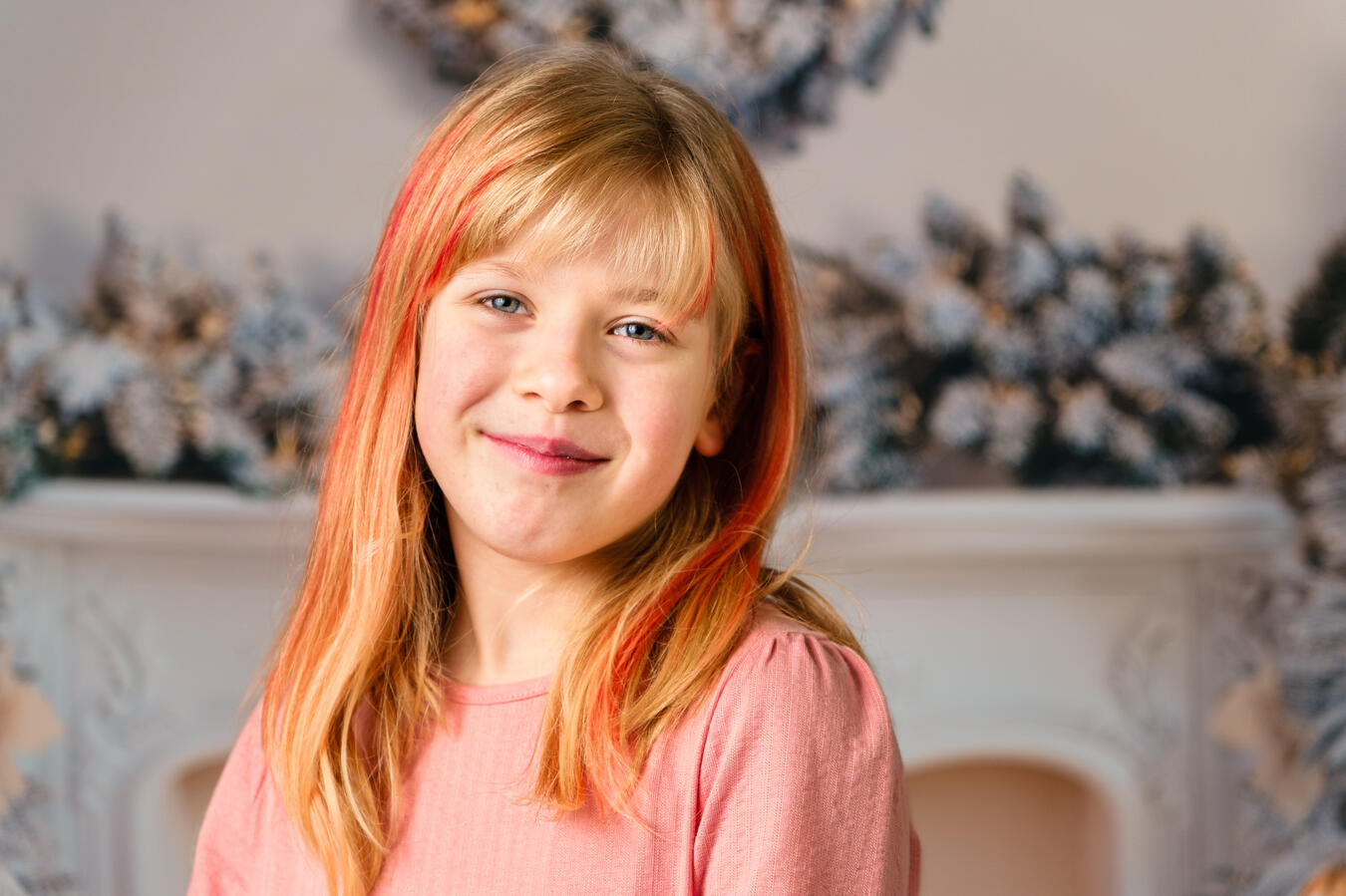 Porträt eines blondhaarigen Mädchens im rosa Pullover vor einer weichen, dekorativen Hintergrundszene.